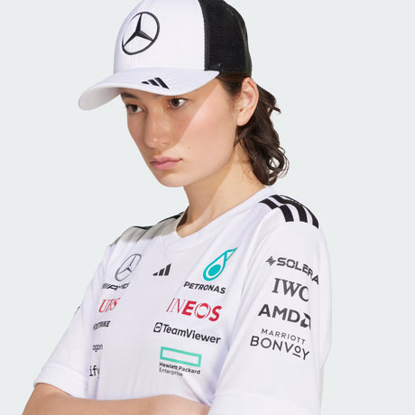 Woman wearing white Mercedes logo T-shirt and cap.