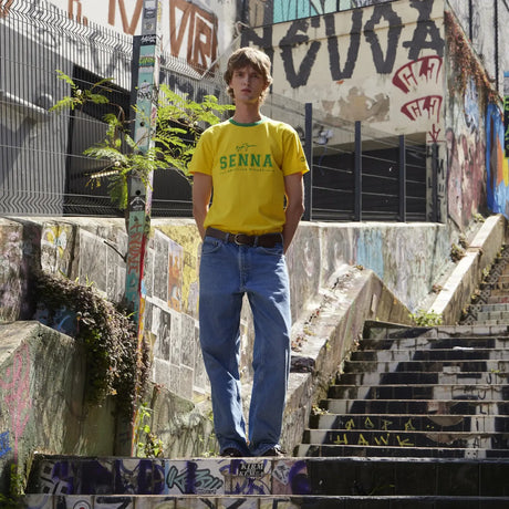 Young man wearing yellow t-shirt standing on stairs in front of graffiti wall.