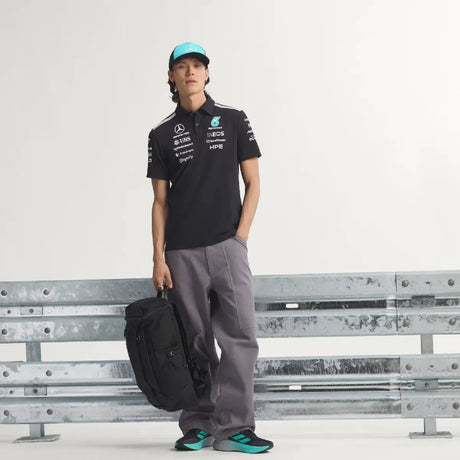 Person standing wearing black t-shirt with cap and bag.